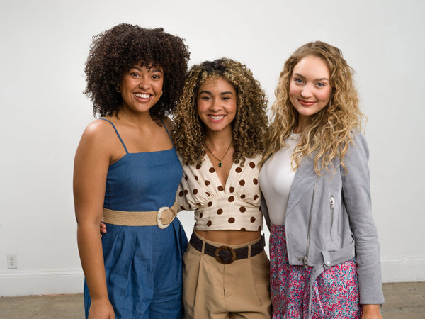 Three smiling women with curly hair on a white background