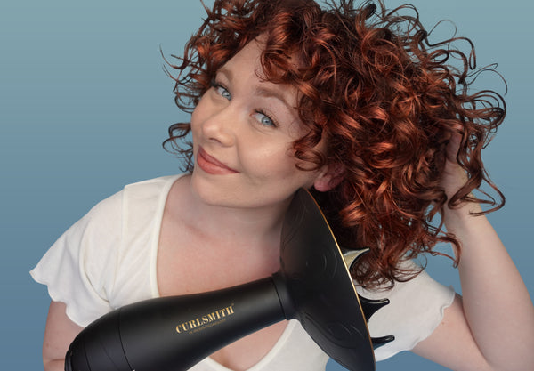 Woman styling her hair with a Curlsmith diffuser on a blue background