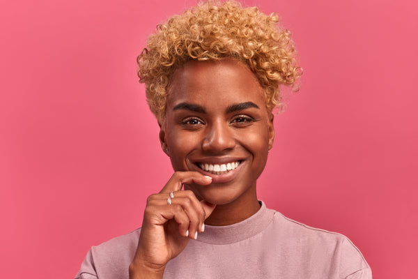 Smiling person with coily hair on a pink background